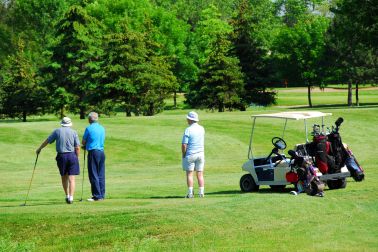 Three senior men on golf course with a golf cart